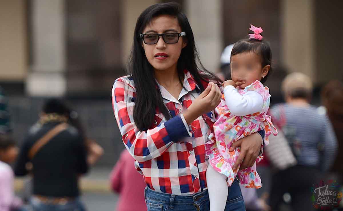 Mujer con su hija en brazos caminando por una calle del Edomex
