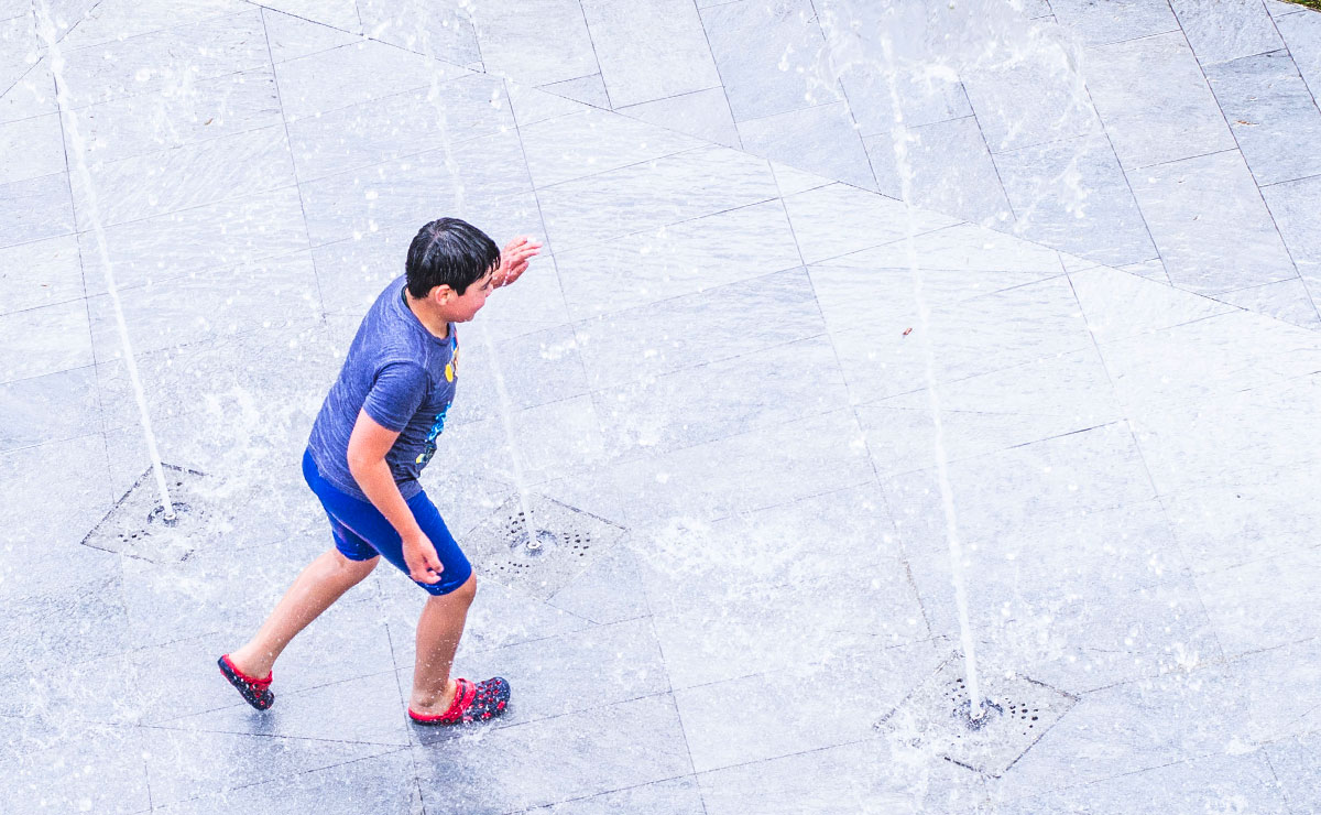 Niño jugando entre las fuentes en tiempo de calor