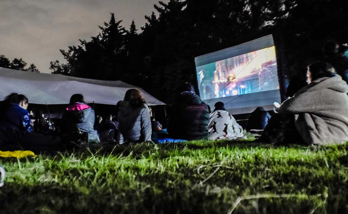 Personas sentadas en el pasto viendo una película en Teotihuacán